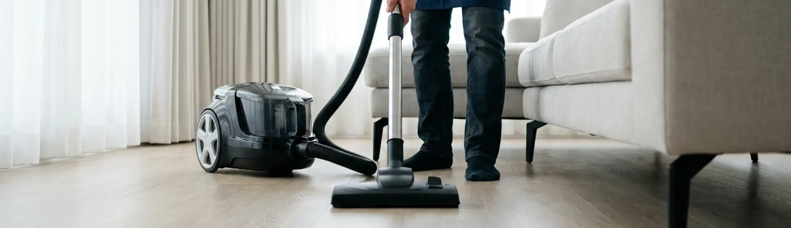 Professional house cleaner vacuuming a living room floor with a canister vacuum cleaner, Boulder, CO.
