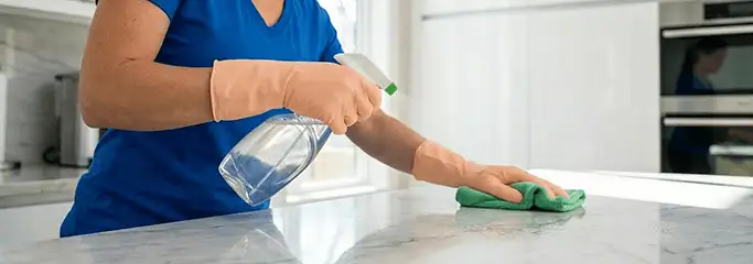 Maid service worker spraying and wiping a kitchen countertop with a microfiber cloth for sanitizing, Boulder, CO.