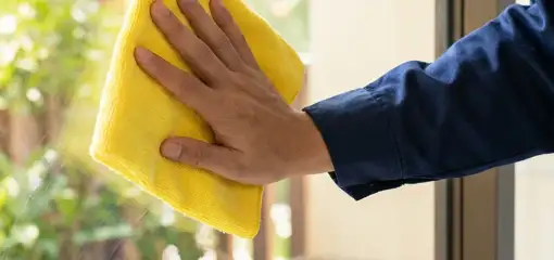 House cleaner wiping a glass window with a yellow microfiber cloth for streak-free cleaning, Boulder, CO.